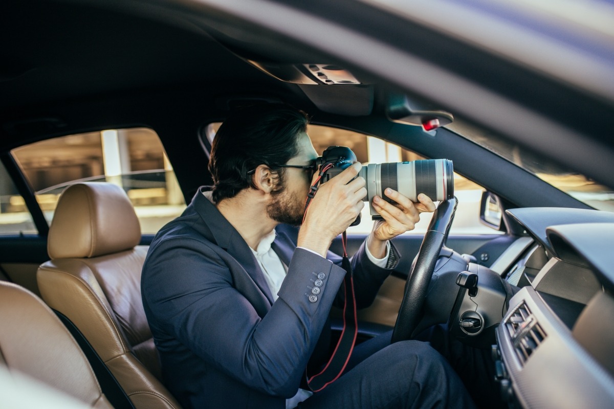 A private investigator set up on surveillance inside a vehicle using a camera